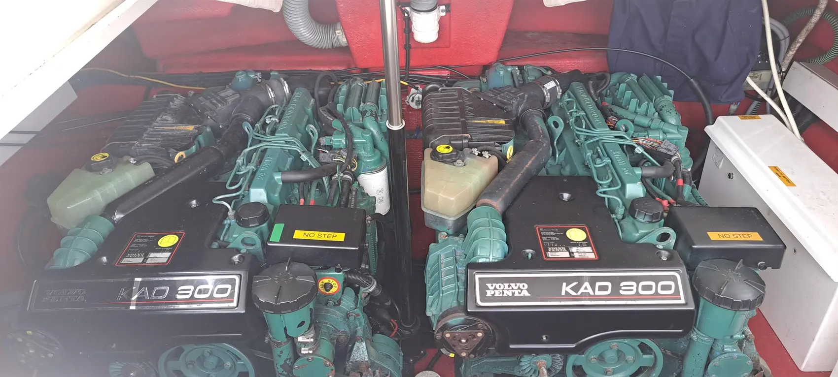 Two Volvo Penta KAD 300 marine engines installed in a boat, with warning labels and various hoses visible in a red compartment.